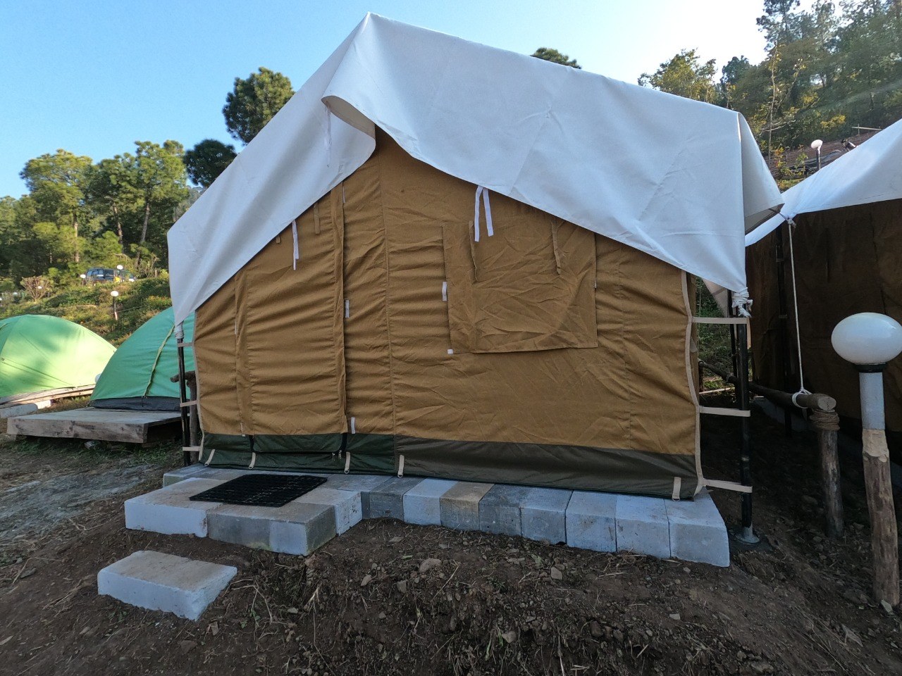 Brown canvas fixed tent on raised stone platform next to green dome tent at The Glide Inn